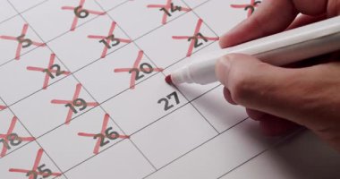 Takvimdeki tarihleri silmek için kırmızı işaret kullanan kişi geri sayımı ya da günleri takip etmeyi işaret ediyor. Resim beklenti, hedef ayarlama ve zaman yönetimini betimler.