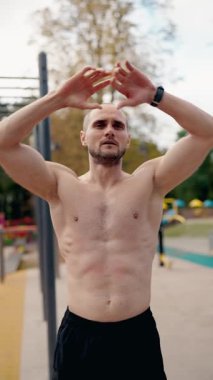 Kaslı bir adam dışarıda çalışmak için ısınıyor. Kollarını kaldırıyor, kaslarını esnetiyor ve vücudunu döndürüyor. Zorlu bir spor seansına hazırlanıyor..