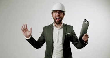 Heyecanlı takım elbiseli ve şapkalı işadamı pano tutuyor, bağırıyor, el sallıyor ve iki parmağını kaldırıyor. Sade beyaz arka planda işyerinde coşku ve başarı gösteriyor. İnşaat için harika.,