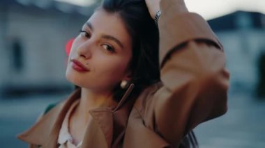 Alacakaranlıkta şehir ortamında duran kendinden emin genç bir kadının portresi. Hafif bir gülümsemeyle kameraya bakıyor, sakin ve kendinden emin olduğunu gösteriyor..