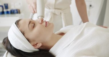 Profesyonel bir kozmetik uzmanı kadın hastalarla güzellik salonunda yüz işlemleri yapar. Güzellik uzmanı ultrason yüz masajı yapıyor. Bir kozmetik terapisti canlandırıcı yüz masajı yapar..