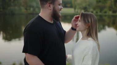 Genç bir çift, doğayla çevrili sakin bir göl kıyısında şefkat ve bağ gösteren şefkatli bir bakışı paylaşıyor. Gölün kenarında huzurlu bir anın tadını çıkaran romantik çift.