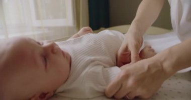 Sevgi dolu anne yeni doğmuş bebeğiyle ilgileniyor. Anne yatağında bebeği için bebek bezi değiştiriyor. Mutlu bebek temizlik yaparken rahattır. Genç anne bez değiştirip bebekle oynuyor..