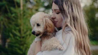 Genç bayan sevimli tüylü köpeğini sakin bir park ortamında nazikçe tutuyor. Evcil hayvanla sahibinin arasındaki bağ çok açık. Sevgi ve arkadaşlığın iç açıcı bir sahnesi yaratıyor..