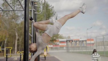 Spor giyim sektöründe formda genç bir kadın halka açık bir spor salonunda baş aşağı asılı duruyor. Gücünü ve esnekliğini gösteriyor. Açık havada Hava Akrobasisi Yapan Atletik Kadın
