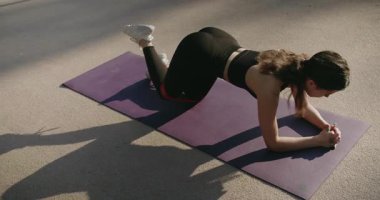 Spor giyinen atletik kadın egzersiz yapıyor, direniş bandıyla tahtada kalın ve bacağınızı kaldırın. Sportif kadın dışarıda egzersiz minderinde çalışıyor. Yoga yapan bir kadın. fitness elastik bant.