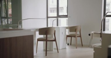 Zarif ve minimalist manikür salonu içinde şık sandalyeler, parlak beyaz tezgahlar ve doğal ışık için geniş pencereler var. Çivi Tasarım İstasyonlu Modern Güzellik Salonu