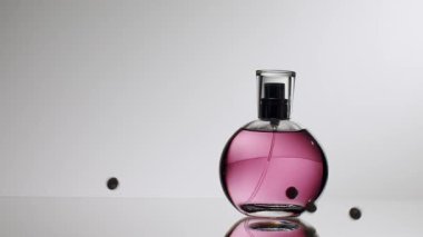 Mor sıvıyla dolu şık, yuvarlak bir parfüm şişesi, dağınık kürelerle yansıtıcı bir yüzeye yerleştirilmiş. Minimalist tasarım zarafet ve entelektüellik taşır. Zarif Parfüm Şişe