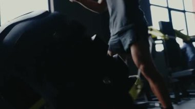 Kaslı bir adam, loş bir spor salonunda yoğun bir çalışma sırasında ağır bir lastiği kaldırıyor. Güçlü Antrenman için Spor Salonu 'nda Ağır Lastik Kaldıran Adam. Spor Salonunda Ağır Lastik Kaldıran Adam