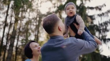 Bebekli genç bir aile açık havada güneşli bir günün tadını çıkarıyor. Huzurlu bir orman ortamında ebeveynler çocuklarına gülümsüyor. Orman pikniğinde güzel bir günün tadını çıkaran genç bir aile.