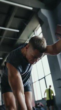 Çağdaş bir spor salonunda dambıllarla çalışan atletik bir adam. Modern ekipman ve büyük pencerelerden gelen doğal ışık ile çevrili kuvvet eğitimine giriyorlar. Dikey