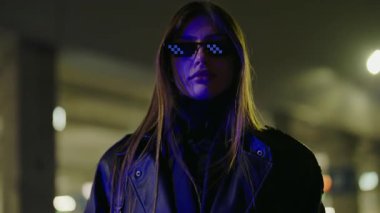 Deri ceket giyen genç bir kadın şık marka güneş gözlükleriyle fotoğraf çekimi için poz veriyor. Modern bir kadın. Profesyonel mankenin yüzü. Genç, lüks, seksi kadın. Dışarıdaki kameraya bakıyor.