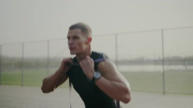 Açık havada antrenman yaparken direnç bantlarını esneten odaklanmış genç erkek sporcu. Fitness, sağlık ve azim iş başında. Genç adam dışarıda egzersiz yaparken direnç bantları takıyor.