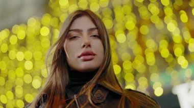 Bokeh arka planında çekici bir kadın portresi. Şehir ışıklarıyla caddede dikilirken kameraya bakan güzel bir kadın model. Akşamları genç ve güzel bir kadının portresi..