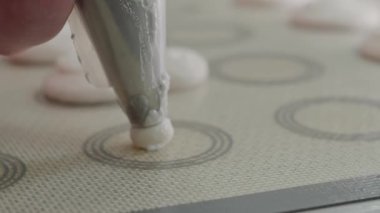 Profesyonel bir pasta şefinin silikon fırın paspasının üzerine ustaca krema dökerek ticari mutfak ortamında leziz tatlılar hazırlarken yakın plan görüntüsü. Pasta Şefi El yapımı makarnaları Hazırlıyor