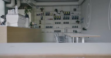 Beyaz duvarları, ahşap aksanları ve düzgün düzenlenmiş ürün rafları olan minimalist bir tasarımı olan modern bir kahve dükkanı. Ortam temiz ve davetkar. Huzurlu bir kahve molası için mükemmel.