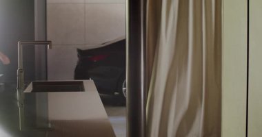 Modern, gölgeli bir mutfak sahnesinde şık bir mutfak adasının önünden geçen bir erkek figürü görülüyor. Modern Mutfakta Çağdaş Tasarımla Yürüyen Adam