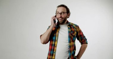 Gözlük takan neşeli genç bir adam ve renkli bir gömlek telefonuyla konuşurken yürekten gülüyor. Beyaz bir stüdyo geçmişine karşı duruyor. Gerçek mutluluğu bulaşıcıdır.,