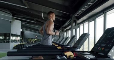 Modern Spor Salonu 'nda Koşu bandına odaklanmış genç adam. Fitness odaklı genç erkek, panoramik pencereli geniş, iyi donanımlı bir spor salonunda koşu bandında koşuyor..