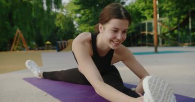 Genç bayan dışarıda egzersiz yapıyor ve esneklik eğitimi veriyor. Siyah giysili güzel bir kadın yoga egzersizi yapıyor. Esnek, ince, genç bir kız antrenman yapıyor..