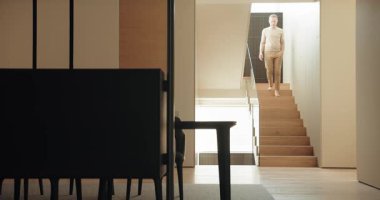 Orta yaşlı bir adam, modern iç tasarım ve huzurlu ev hayatını yansıtan şık minimalist bir evde merdivenlerden iniyor. Modern Ev Tasarımında Alt katta Yürüyen Adam