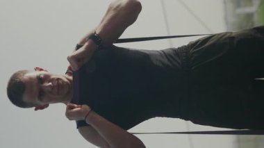 Adanmış erkek sporcu dışarıda çalışmak için direniş bantları kullanıyor. Fitness ve şehir yaşam tarzına odaklan. Şehir Arkaplanı 'nda direniş gruplarıyla egzersiz yapan genç adam. Dikey video.