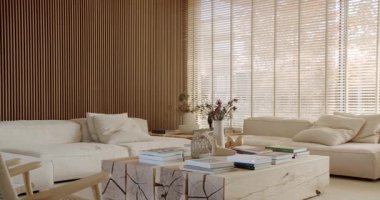 Modern oturma odasının içinde ahşap duvar panelleri, büyük pencereler ve iki beyaz kanepe var. Kitaplar doğal ahşap sehpanın üzerine istiflenmiş şık ve rahat minimalist bir ev yaratıyorlar..
