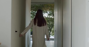 Bir kadın koridorda yürür ve dışarıya bir kapı açar, ağaçların manzarasını gözler önüne serer. Çizgili, bol bir gömlek giyiyor. Bu an bir huzur ve sükunet hissi uyandırıyor..