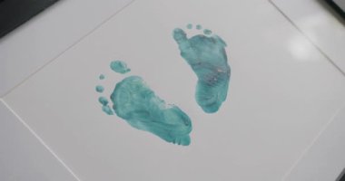 Beyaz arka plan kağıdındaki bebek ayaklarının yeşil izleri. Çizim için yaratıcı bir fikir. Titiz insan ayak izleri, gri yüzeyde yeşil boya ile ustalıkla işlenmiş..