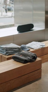 Basit ahşap mobilyalarda, kot pantolonda, cekette ve raflarda sergilenen katlanmış günlük giysiler. Modern mağaza içi büyük vitrinli, kaykaylı pencere pervazlı, şehir manzaralı