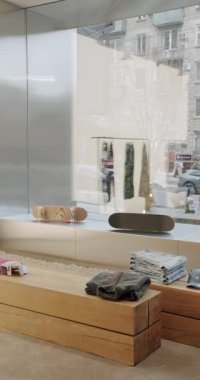 Ahşap banklarda kaykay ve giysi sergilenen şehir içi moda mağazası. Büyük pencereler şehir yaşamını ve elbise raflarının yansımalarını gösteriyor. Minimalist tasarım