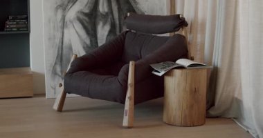 Ahşap bacakları ve yumuşak yastıkları olan modern bir koltuk. Rahat bir sandalyesi, ahşap sehpası ve bir kitabı olan şık bir kitap odası. Konforlu ve rahatlatıcı ev atmosferi.