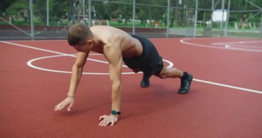 Atletik adam dışarıda yoğun antrenman yapıyor ve çapraz antrenman yapıyor. Açık hava fitness parkı. Kaslı bir adam spor sahasında çapraz antrenman ve omuz vuruşuyla kalas egzersizi yapıyor..