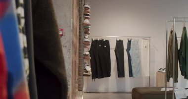 Perakende mağazasında giysi ve ayakkabıların yakın çekimi. Mağazanın modern, endüstriyel bir tasarımı, tuğla duvarları ve metal aksesuarları var. Elbiseler askılarda ve raflarda sergileniyor.,