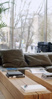 Ahşap masa, kanepe, kitap ve şehir manzaralı modern oturma odası iç tasarımı. Doğal ışık odayı dolduruyor. Sıcak ve davetkar bir ortam, rahatlamak için mükemmel. Şık şehir dekorasyonu.