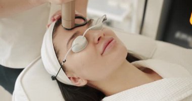 Koruyucu gözlüklü güzel bir kadın, bir tıp merkezinde lazer yüz tedavisi gören genç bir kız, cilt gençleştirme konsepti.