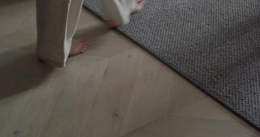 Ahşap bir zemin ve insan ayaklı dokuma bir kilimin olduğu rahat bir evin yakın çekimi. Halıların yanındaki ahşap zeminde çıplak ayaklarla yürüyorum.