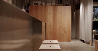 Bir giyim mağazasının modern ve minimalist iç tasarımı. Ilık ahşap paneller, parlak metal tezgah ve yumuşak ışıklandırma sofistike bir atmosfer yaratır. Doğal malzemeler ve temiz çizgiler.