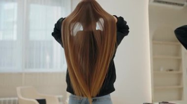 Uzun, düz kahverengi saçlı genç bir kadın parlak bir salonda kameraya arkası dönük duruyor. Ellerini saçlarının arasında gezdiriyor, özgürce akmasına izin veriyor. Odaklandığımız konu sağlık.,