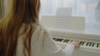 Genç kız evde piyano çalışıyor. Ev müziği stüdyosu kadını. Müzik eğitimi. Eller piyano tuşlarına basıyor. Nota okuyorum. Piyano öğrenme dersleri. Öğrenim ve öğrenim geliştirme kavramı.