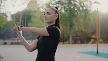 Antrenman sırasında kollarını uzatan odaklanmış genç bir bayan sporcu. Huzurlu bir park ortamında yakalandı. Park 'ta Esneme Egzersizleri Yapan Genç Kadın