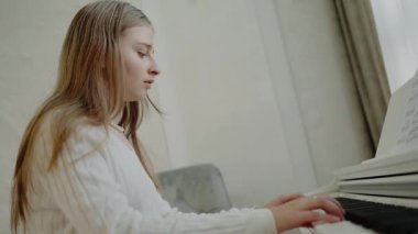Genç kız evde piyano çalışıyor. Eğitim ve öğrenim geliştirme konsepti. Odaklanmış genç, güzel bir kız. Elektrikli piyano çalarak eğleniyor. Nota okuyorum. Piyano öğrenme dersleri