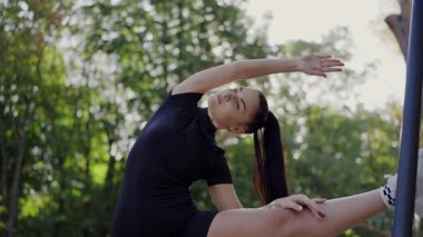 Genç bir kadın, sakin yeşil bir parkta yoga yaparken esneyerek esneklik ve rahatlama gösteriyor. Peaceful Park 'ta Yoga Çalışan Genç Kadın