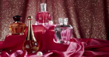 Pembe kumaş ve incilerle süslenmiş zarif parfüm şişelerinin bir derlemesi, ışıl ışıl bir arka planda. Lüks, güzellik ve moda temaları için mükemmel. Pembe Kumaşta Zarif Parfüm Şişeleri