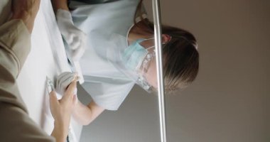 Manikürcü, kadın manikürü sırasında manikürcüyü ustalıkla şekillendirmek ve rafine etmek için manikür dosyası kullanıyor. Maskeli manikürcü ve eldivenli kadın tırnaklarını güzellik salonunda törpülüyor. Spa tedavisi. Dikey video.