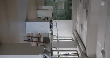 Modern bir güzellik salonunun parlak ve gösterişli bir iç mekanı. Şık beyaz çalışma istasyonları ve büyük pencerelerden gelen doğal ışık. Dikey video.