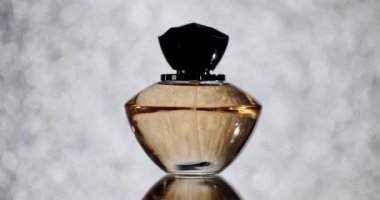 Parlak bir arka planda siyah kapaklı zarif bir parfüm şişesi lüks, sofistike ve cazibeyi çağrıştırıyor. Güzellik, moda ve zarafet kavramları için ideal görüntü.