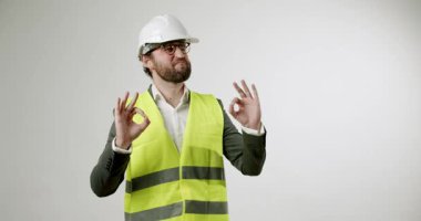 Sıkı bir şapka ve güvenlik yeleği giyen neşeli bir inşaat mühendisi ya da mimar iki eliyle sağlam beyaz arka plan üzerinde 