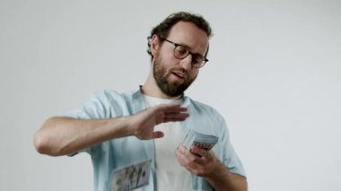 Gözlüklü bir adam ağır çekimde havaya para fırlatıyor. Elinde bir yığın yüz dolarlık banknot tutuyor ve birazını havaya fırlatıyor. Mutlu, zengin ve başarılı görünüyor. Finansal ve iş için mükemmel.,