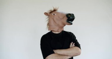 At kafası maskesi takan bir adam kollarını kavuşturmuş duruyor. Etrafına bakıyor, etrafını inceliyor. Duruşu güven ve mizah duygusunu akla getiriyor..